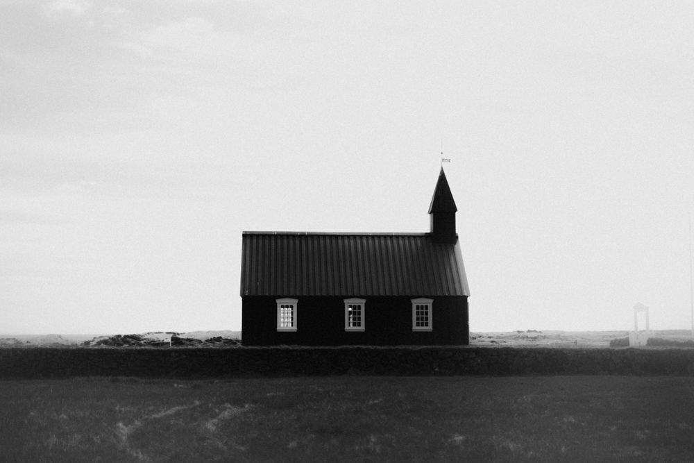 Black and white silhouette of a small church against a moody sky.
