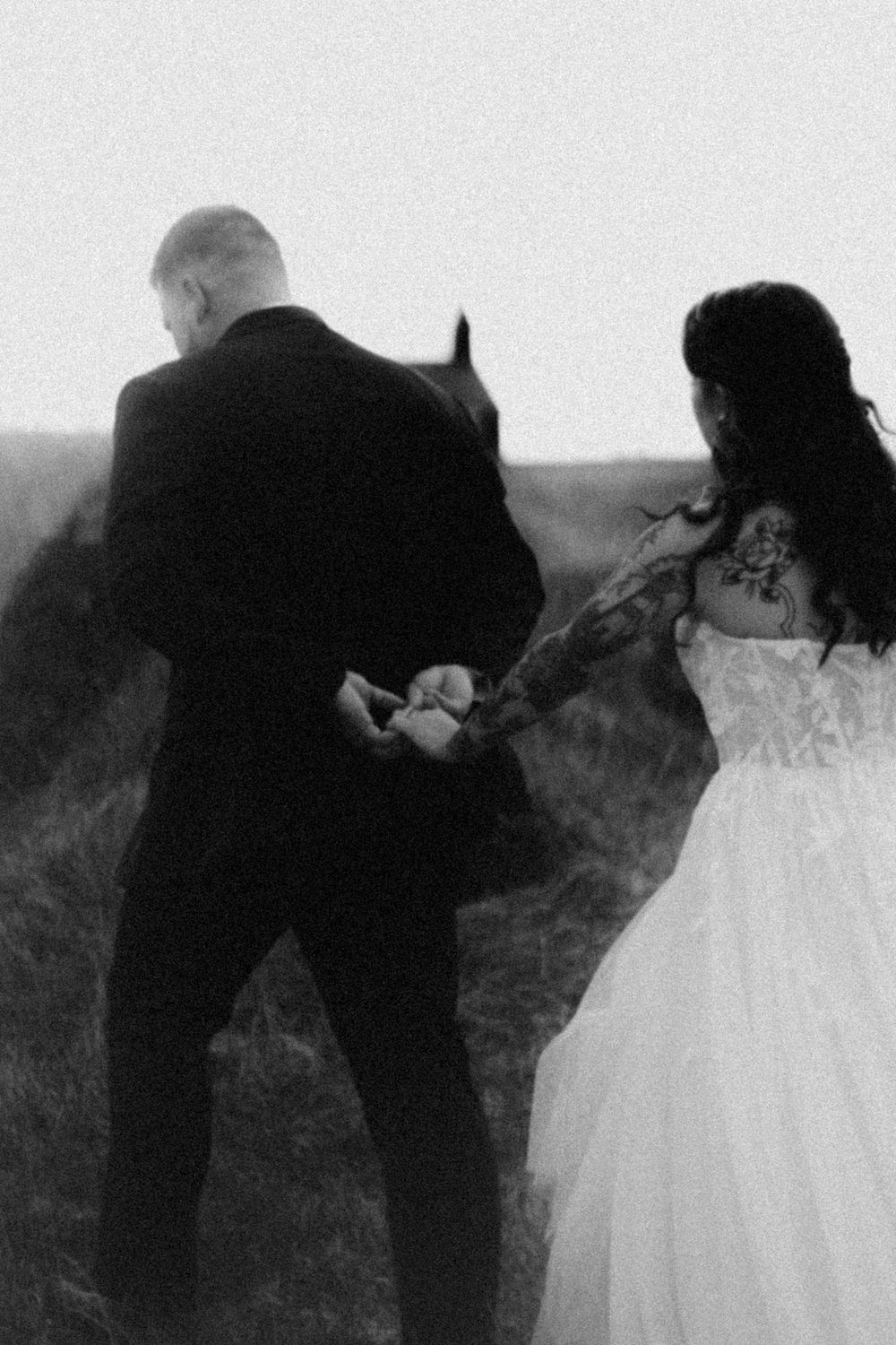A black and white photo of newlyweds holding hands in a misty field with a church silhouette.