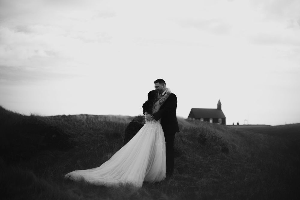 Silhouetted wedding couple embracing on a hilltop with a church visible in the distance.