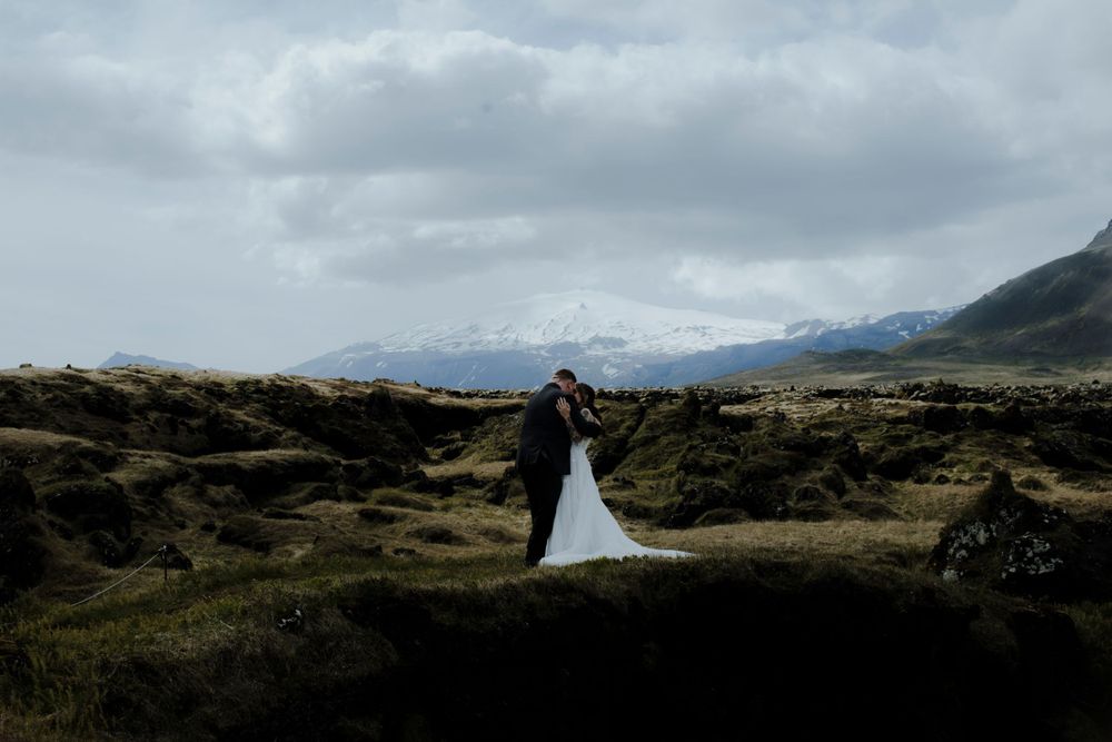 Wedding couple poses against a dramatic mountain landscape with cloudy skies.