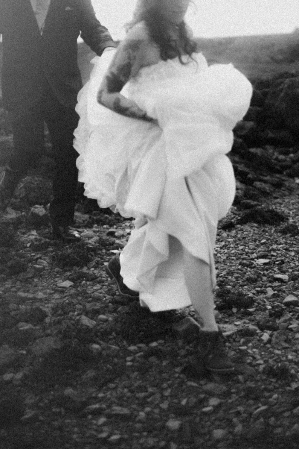 Black and white image of a flowing white wedding dress in motion on rocky terrain.
