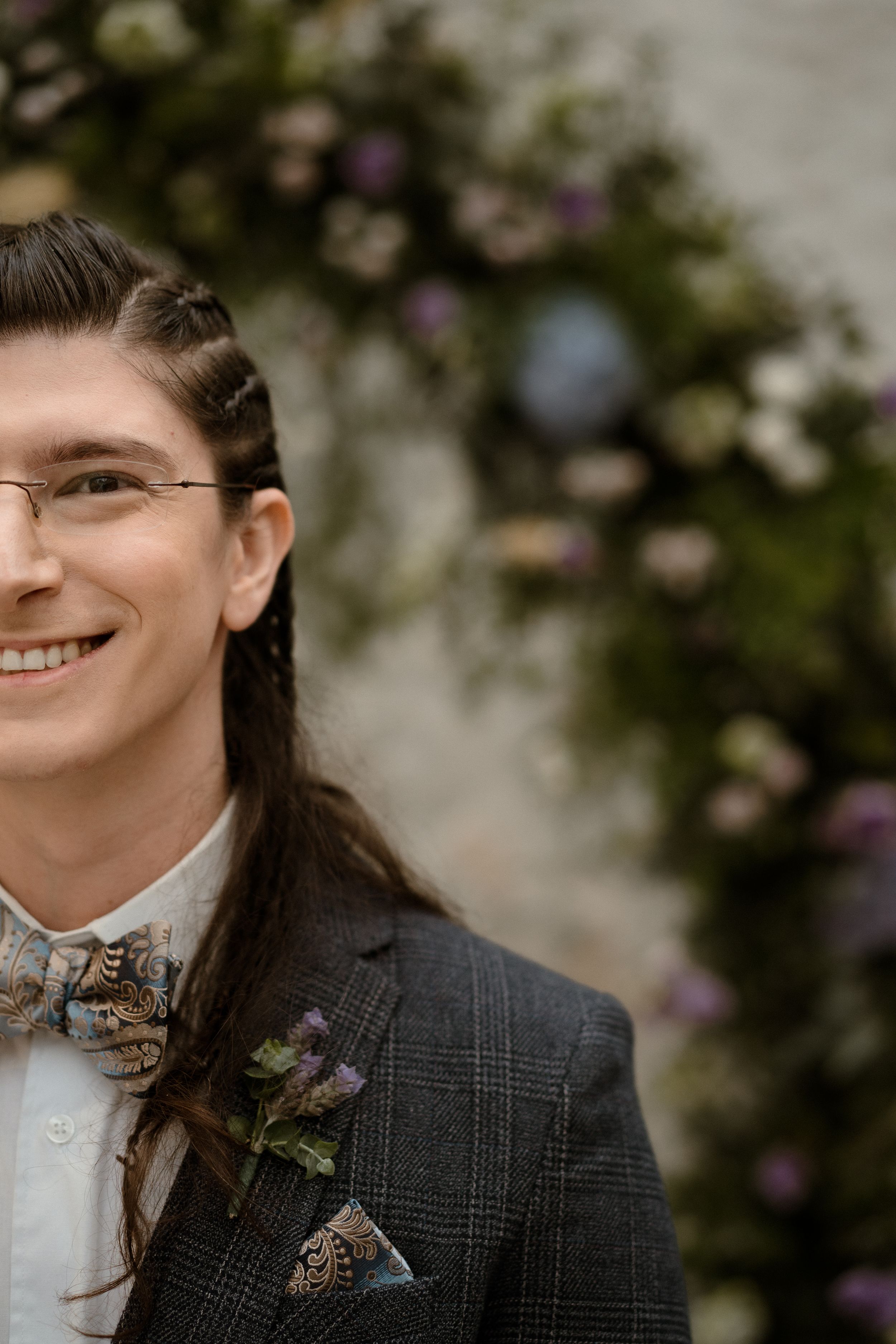 Person wearing plaid suit jacket with bow tie and floral boutonniere.