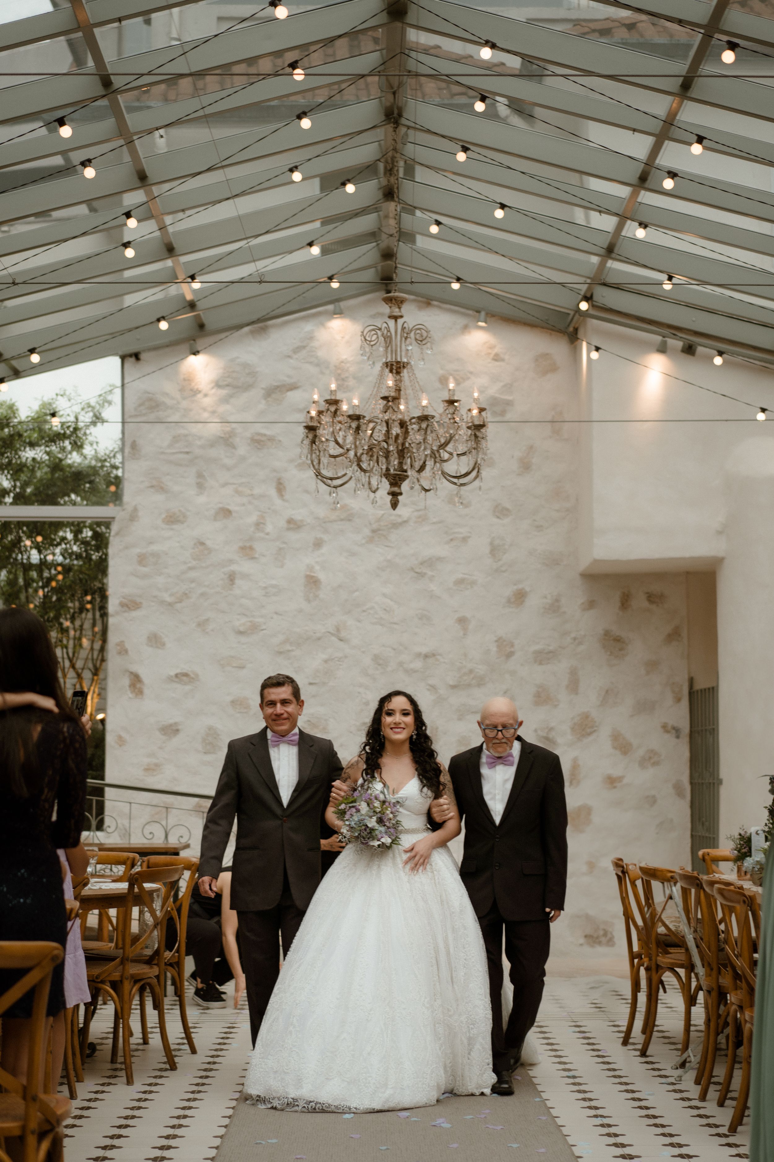 Wedding ceremony in an elegant glass-ceiling venue with stone walls and a vintage chandelier.