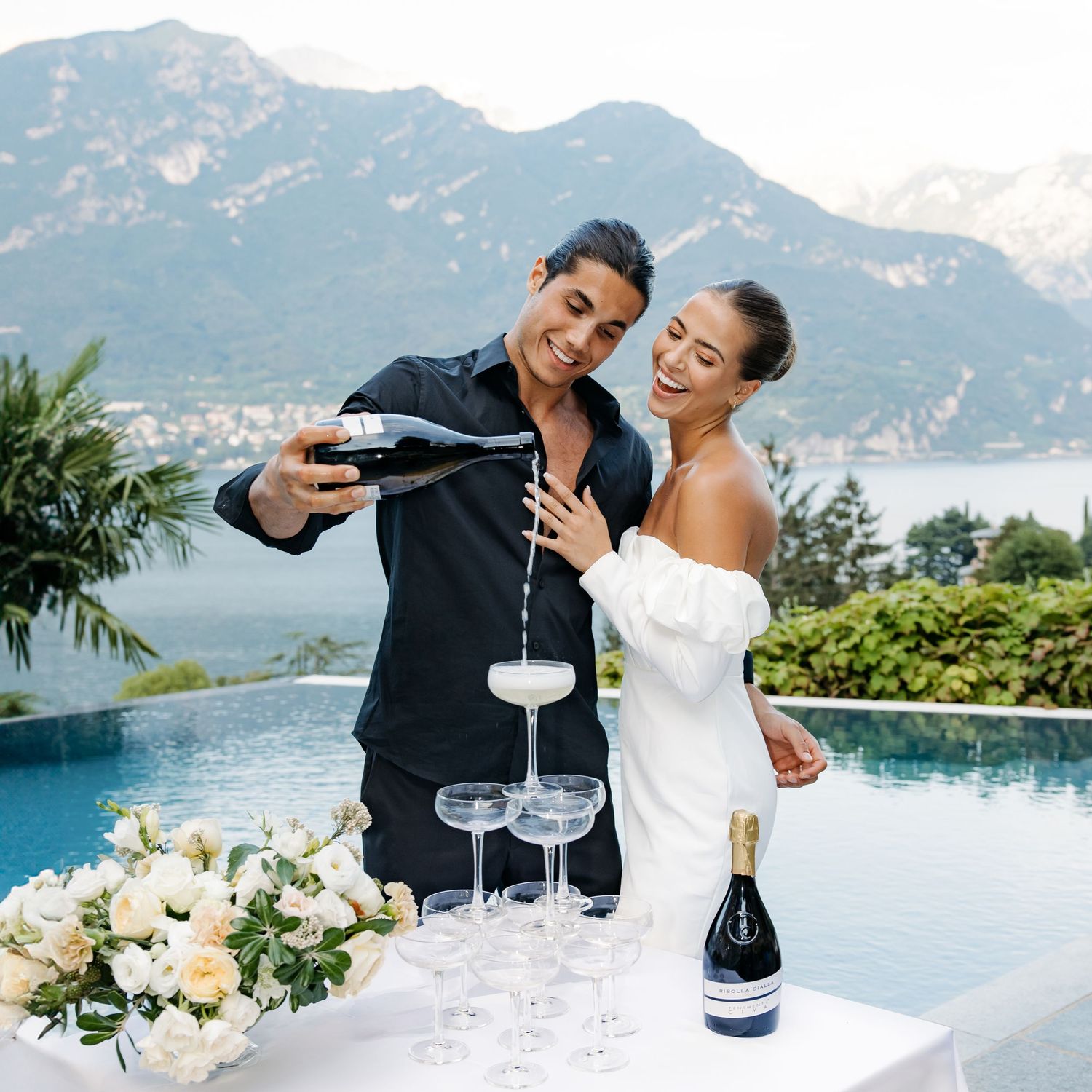 Couple pouring champagne by infinity pool with mountain view in Lake como during engagement photoshoot.