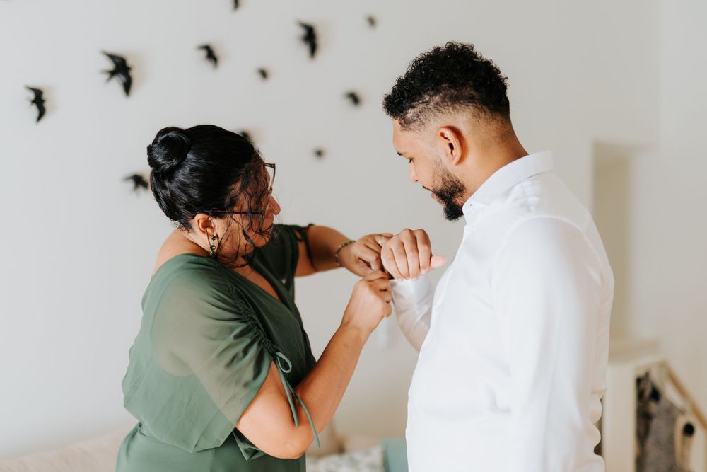 Woman in green dress helping a man in white shirt adjust his cufflinks indoors.
