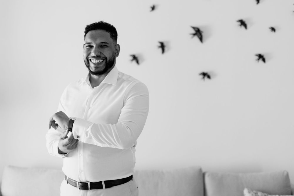 Black and white portrait of a smiling groom in a white shirt adjusting his cufflinks.