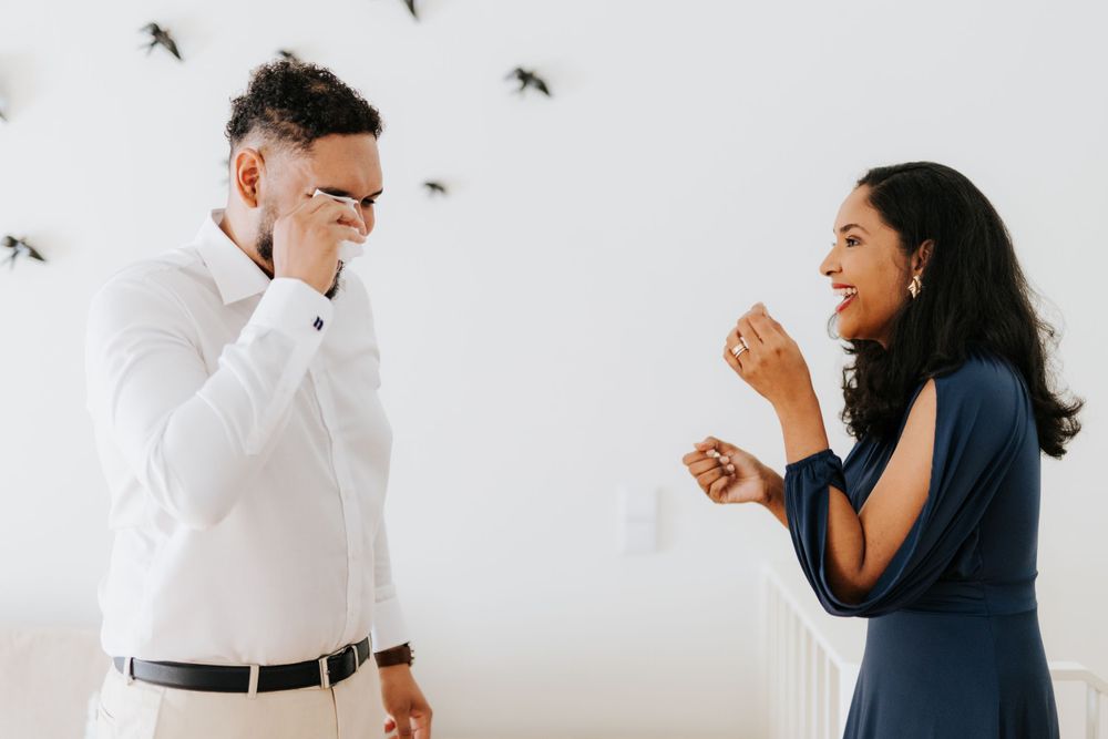 Emotional groom wiping tears while reading wedding vows as bride smiles joyfully.