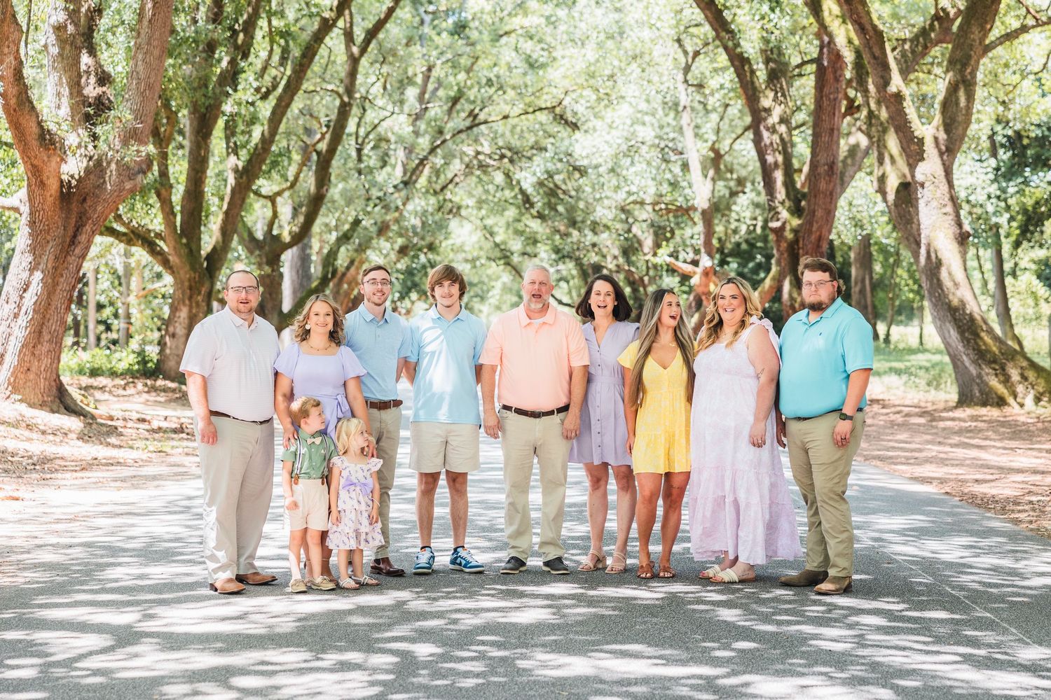 Family group poses together under oak trees in coordinating pastel outfits for outdoor photo session.
