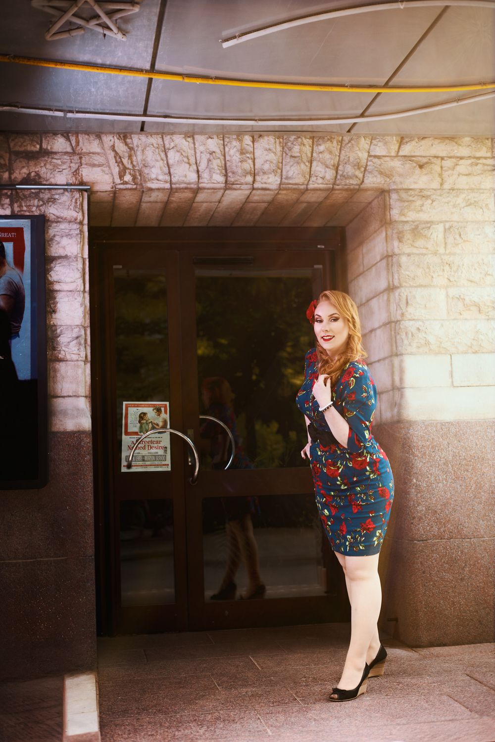 Retro fashion pose against stone building entrance wearing fitted floral dress.
