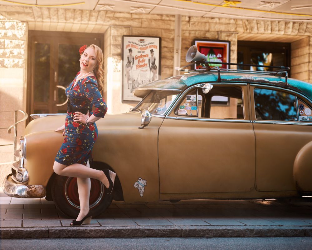 Full length vintage fashion portrait beside classic car with retro styling and urban background.