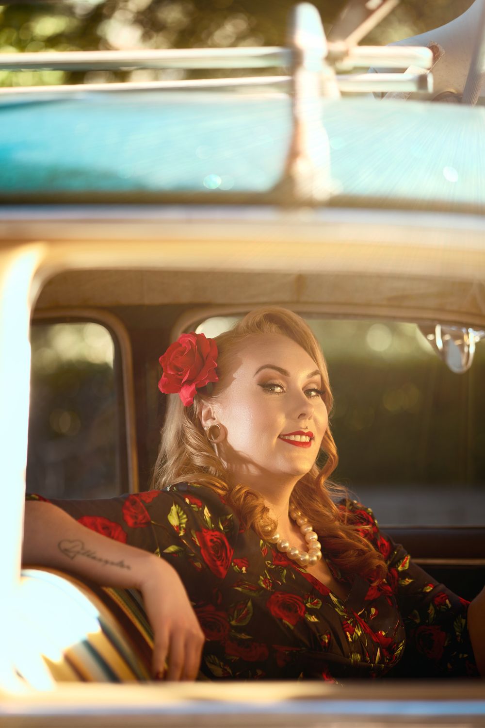 Retro styled automotive portrait through car window featuring floral dress and vintage hair styling.