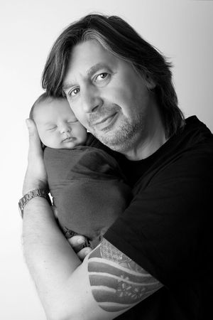 Black and white portrait of an adult holding a sleeping newborn baby against their shoulder.