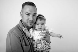 Black and white studio portrait of adult holding smiling infant in patterned outfit.