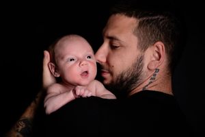 A dramatic dark portrait capturing an intimate bonding moment with a wide-eyed infant.