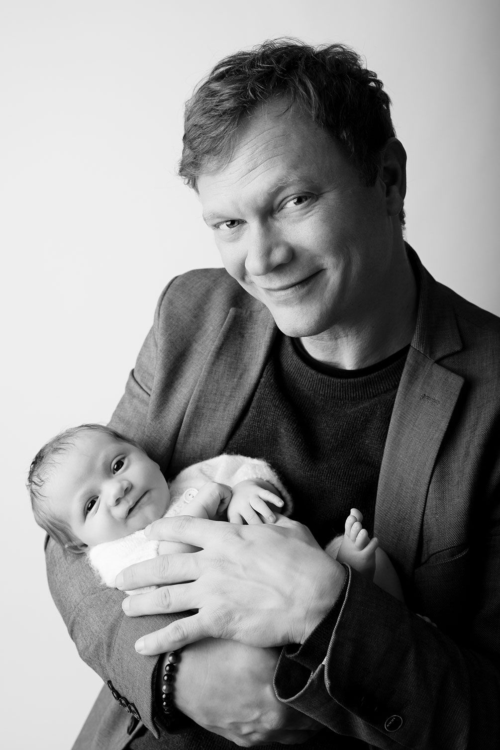 Professional black and white portrait of adult in suit jacket holding peaceful sleeping newborn.