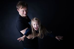 Dramatic studio portrait of adult playfully holding young child against dark background.