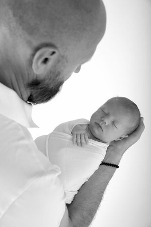 Tender moment captured in black and white as a parent looks down at their sleeping newborn.