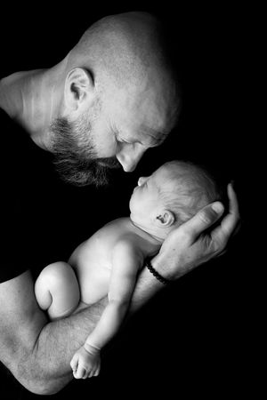 Dramatic black and white portrait of a parent cradling a naked newborn against dark background.