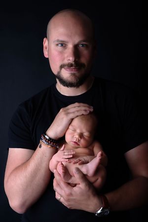 Studio portrait of a parent holding a sleeping newborn against dark background.