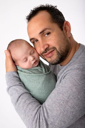 Warm portrait of a parent cuddling their sleeping newborn wrapped in mint green.