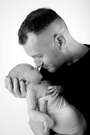 A tender black and white portrait of a parent cradling and kissing a newborn baby.