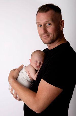 Studio portrait of a parent in black t-shirt holding sleeping newborn against white background.