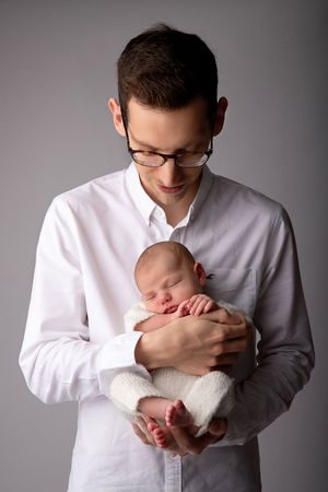 A studio portrait showing a gentle moment between a person in white holding a sleeping infant.