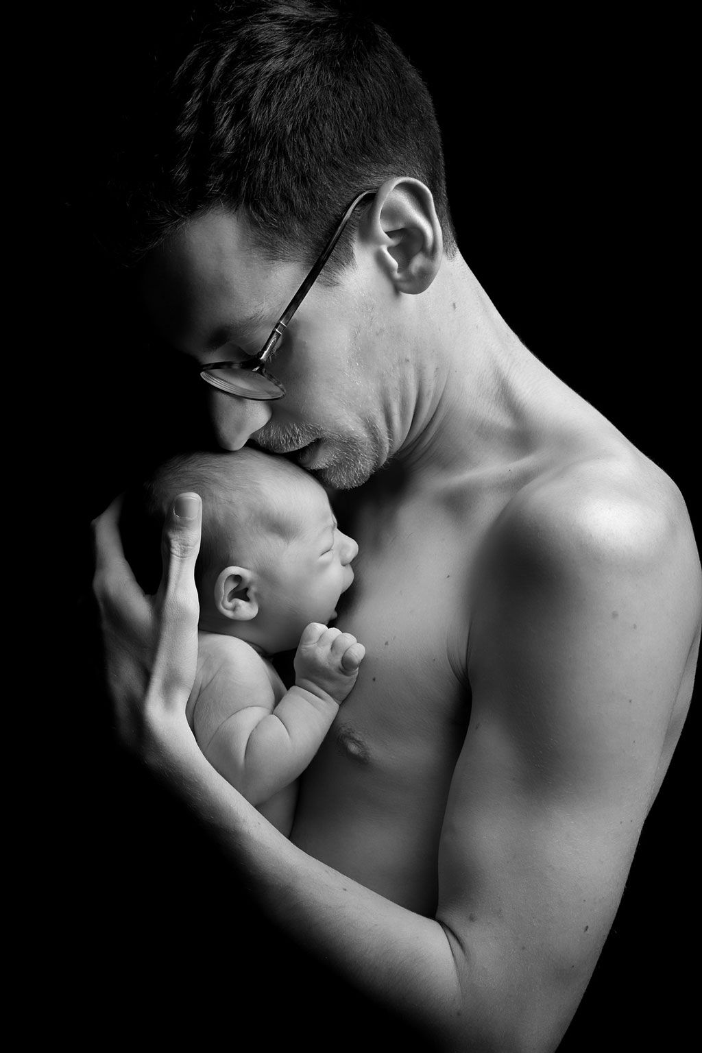 Dramatic black and white portrait showing an intimate skin-to-skin moment with a sleeping newborn.