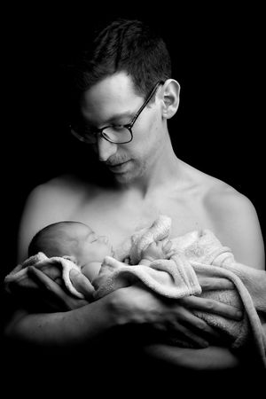 An artistic black and white portrait showing a tender moment with a swaddled sleeping infant.