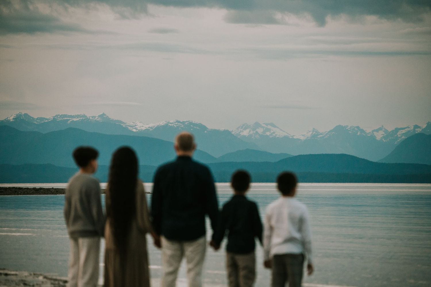 Family holding hands looking out at mountains from Saratoga Beach during blue hour. Photography by Photographer Soulfull Photographs