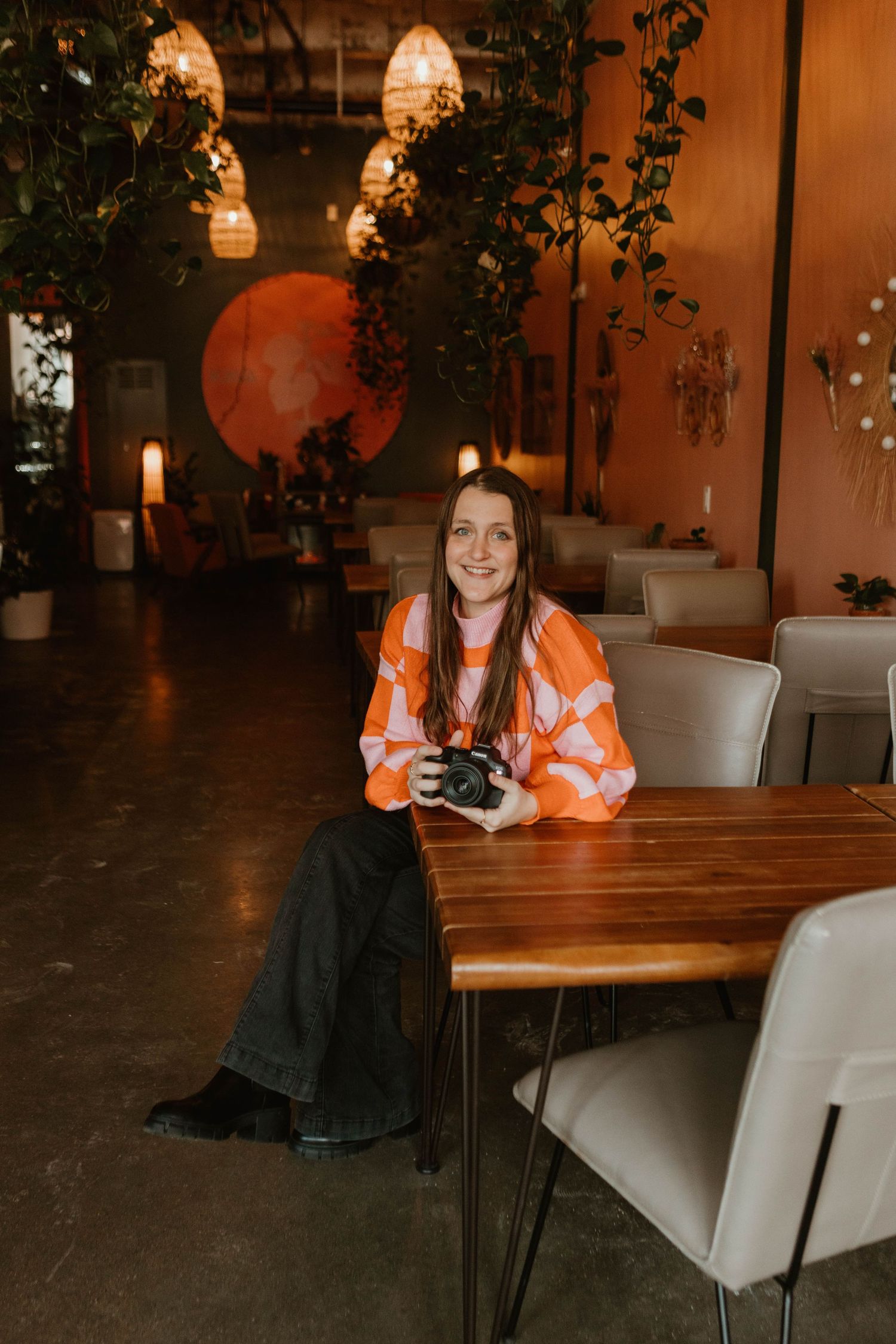 A photographer sits at a wooden table in a cozy restaurant with warm lighting and hanging pendant lamps.
