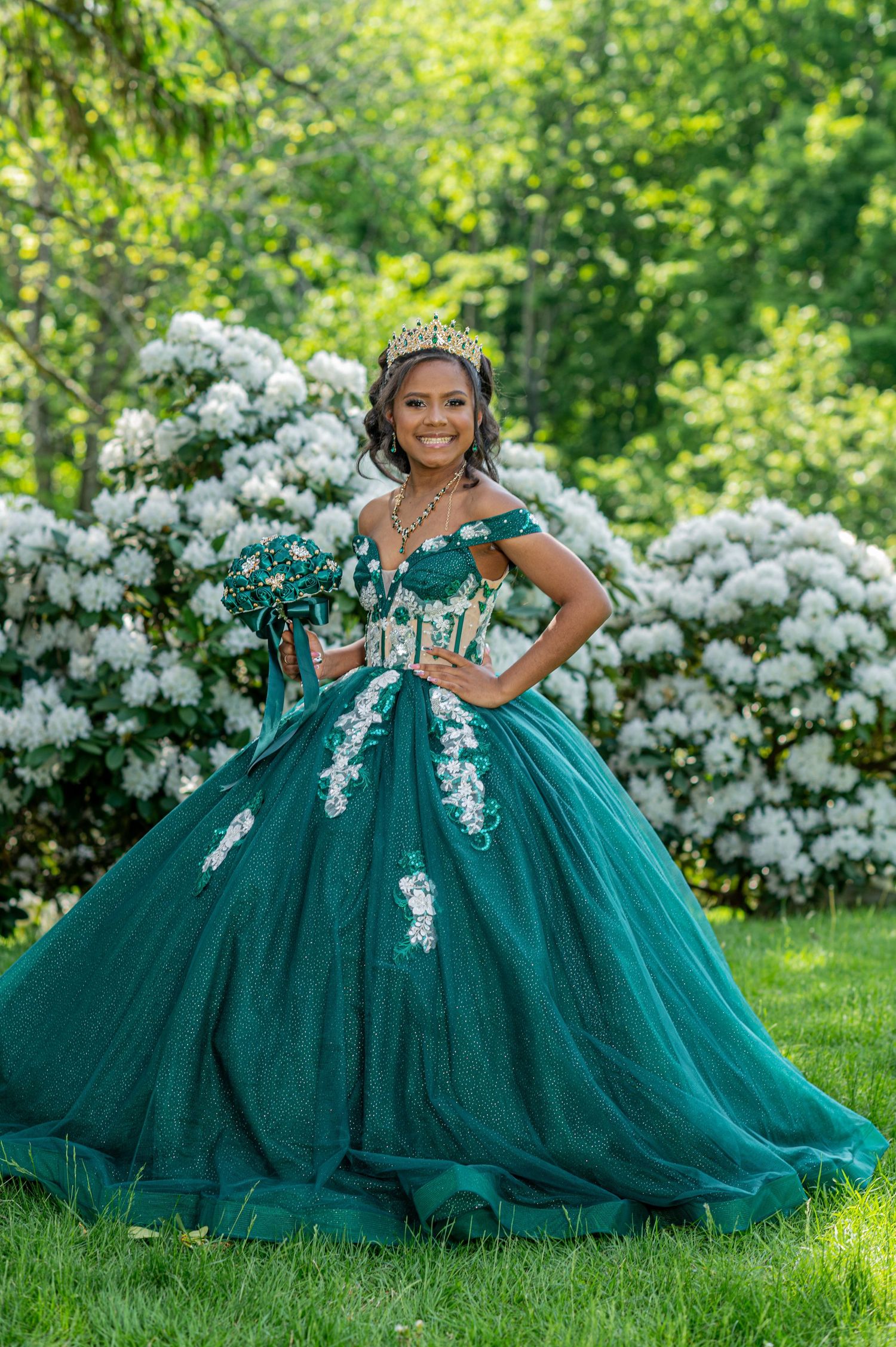 Stunning emerald green ball gown with white lace appliques photographed in a garden with blooming white flowers.