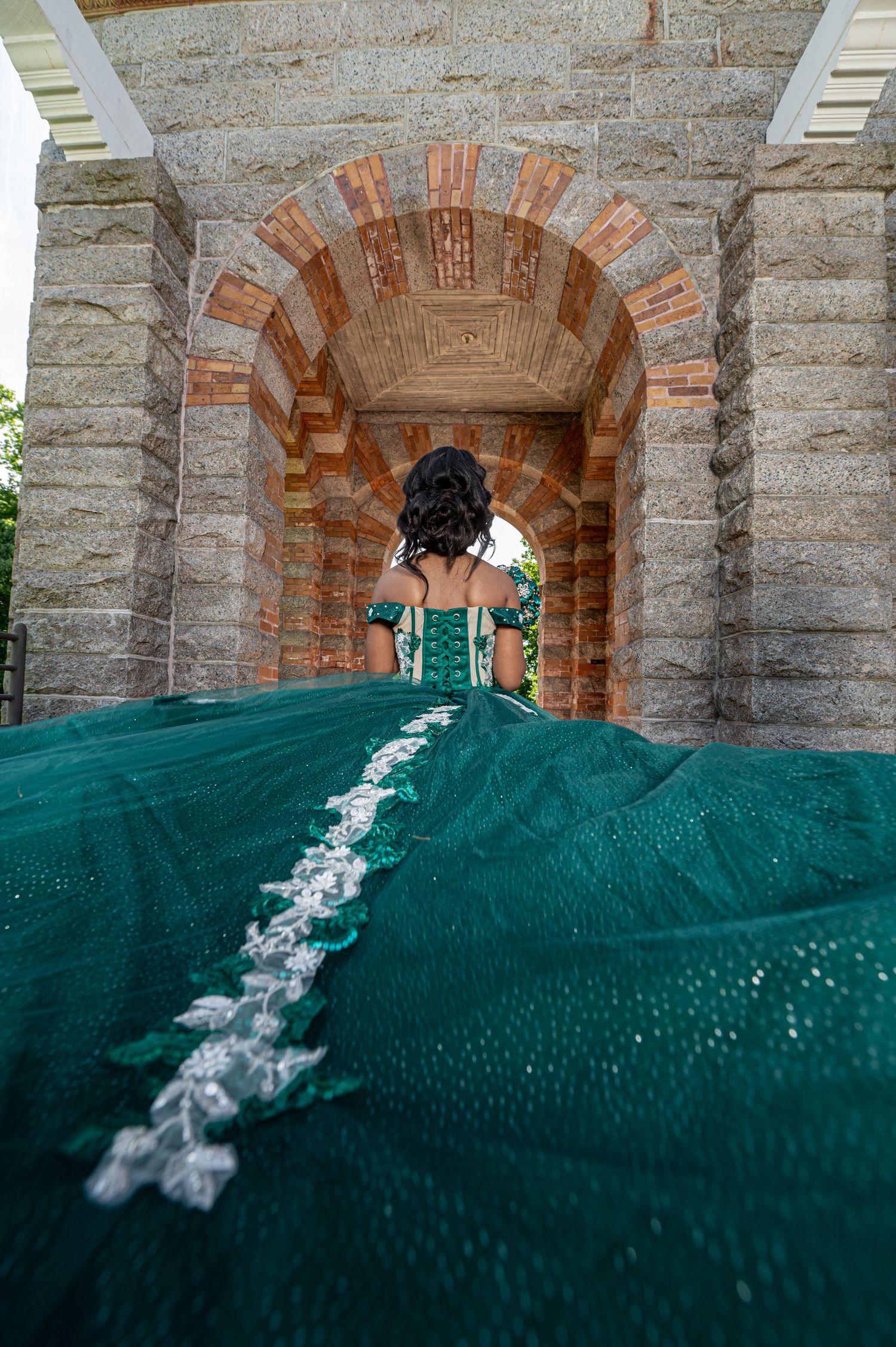 Close-up of emerald green dress train with white lace detail through stone archway.