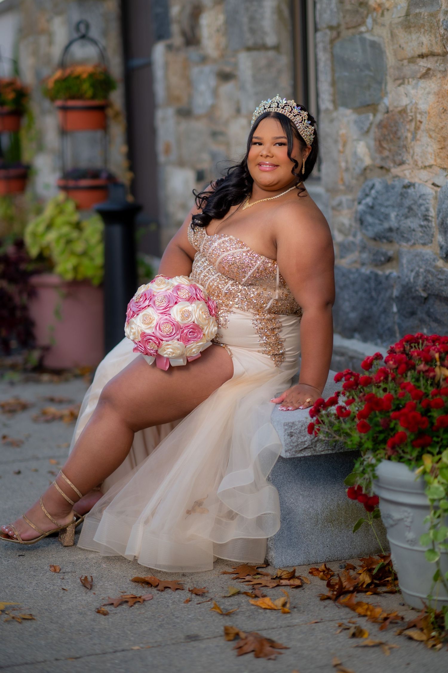Elegant champagne wedding dress with pink floral bouquet photographed against stone wall with autumn flowers.