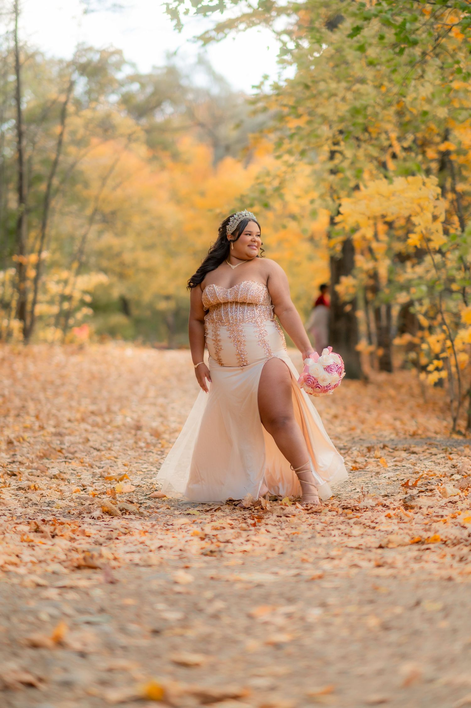 Person in romantic pink tulle dress poses gracefully among autumn leaves in outdoor photoshoot.