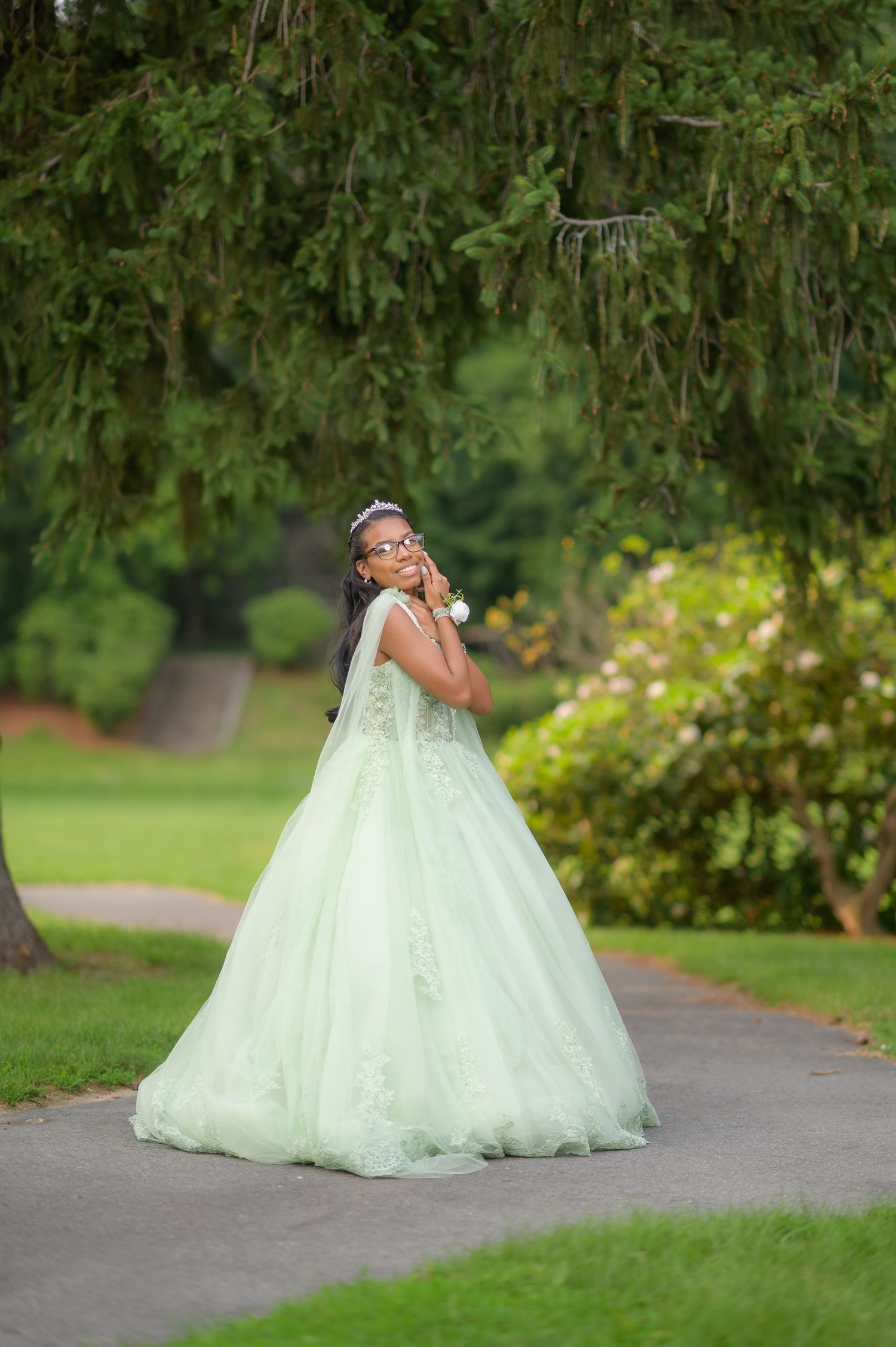 A mint green ballgown wedding dress on display in a lush garden setting.