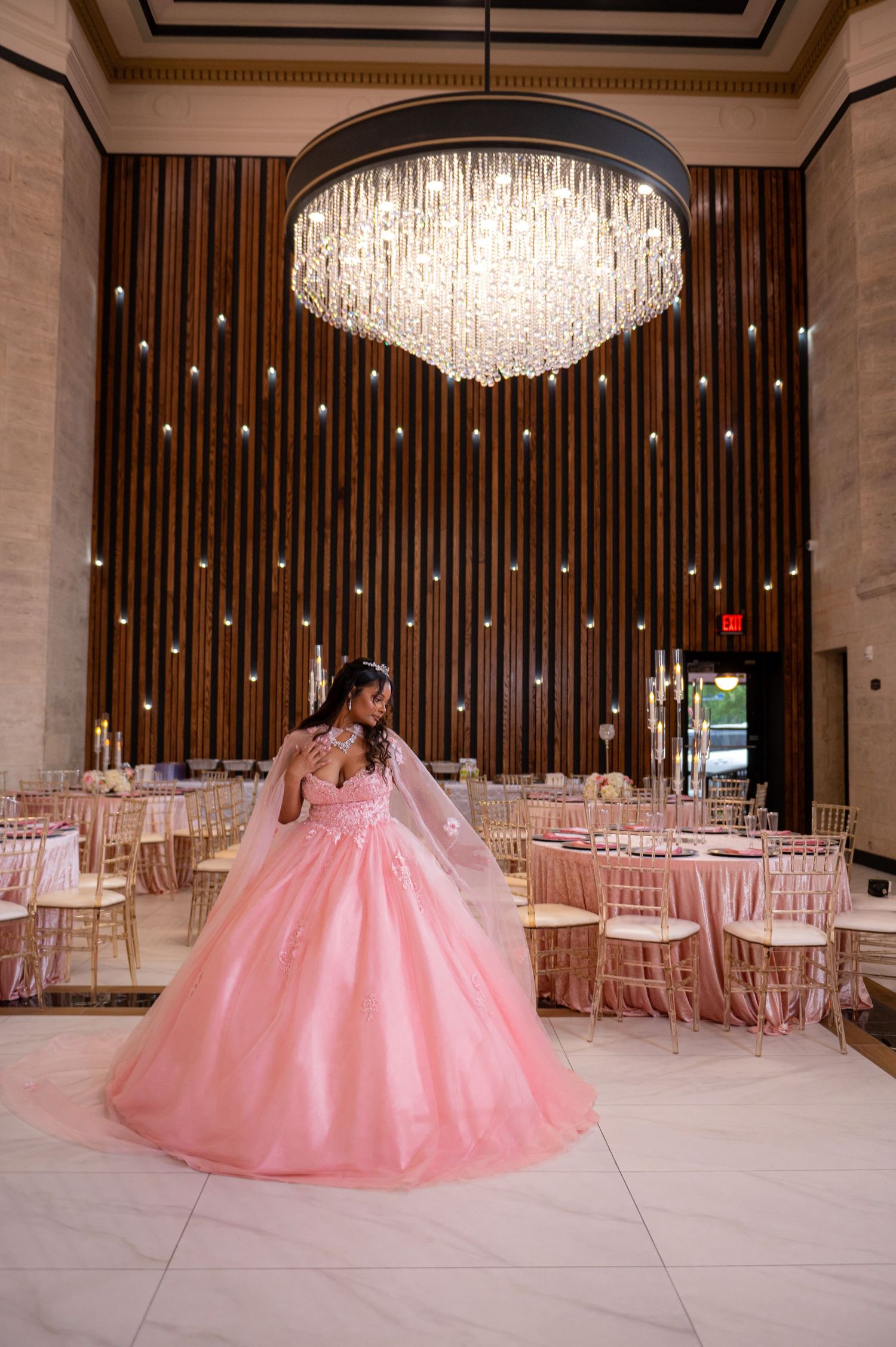 Ballgown silhouette in soft pink photographed under crystal chandelier in elegant reception venue.