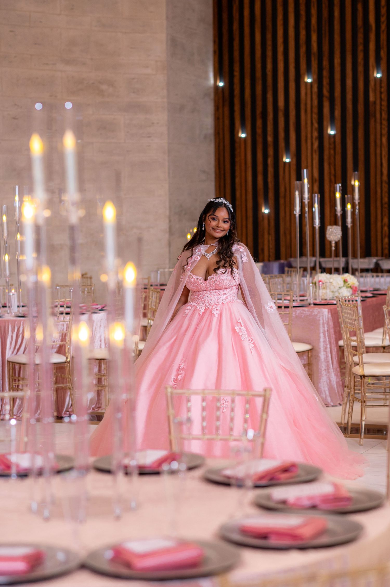 Pink princess ball gown surrounded by candlelit table settings in luxurious venue.