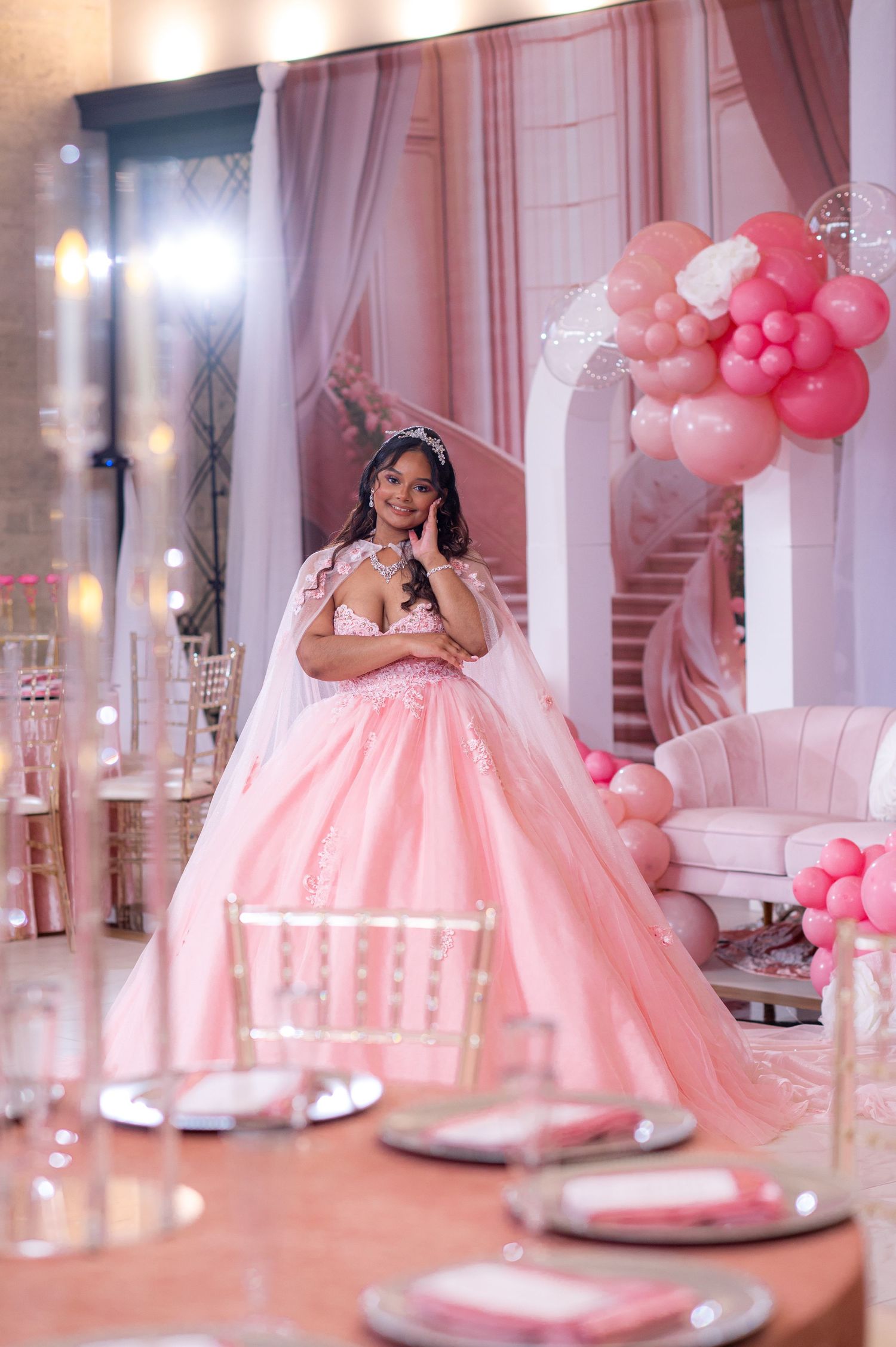 Dreamy pink ball gown photographed in elegant venue with pink balloon arch and table settings.