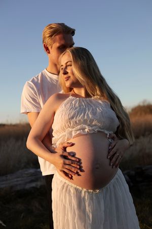 ett par står tillsammans, båda håller om kvinnas gravid mage och mannen kysser kvinnan på huvudet.
