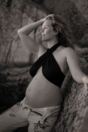 bild på en gravid kvinna som lutar sig mot en klippa. hon har jeans och en svart topp på sig och kollar utåt och handen drar hon genom håret