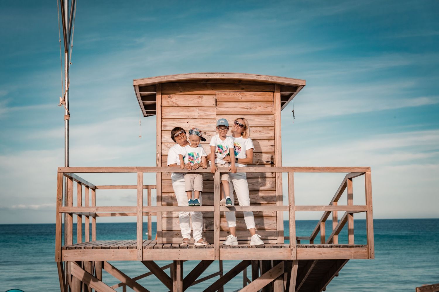 A family posing together on a wooden beach lifeguard tower during a relaxed vacation photo shoot in Mallorca.