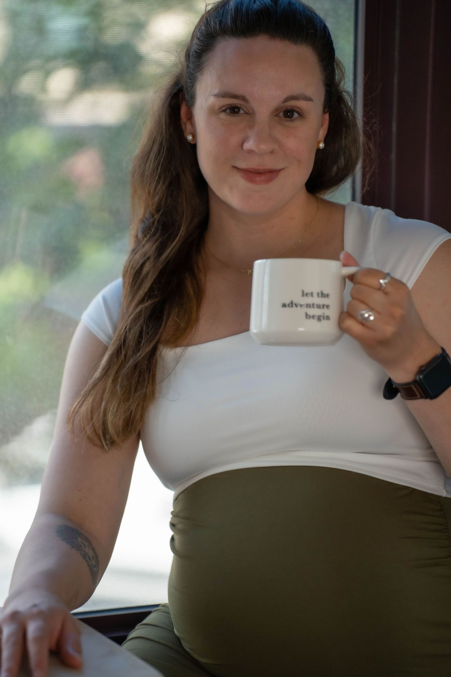 A person in a white top holding a coffee mug while sitting casually.