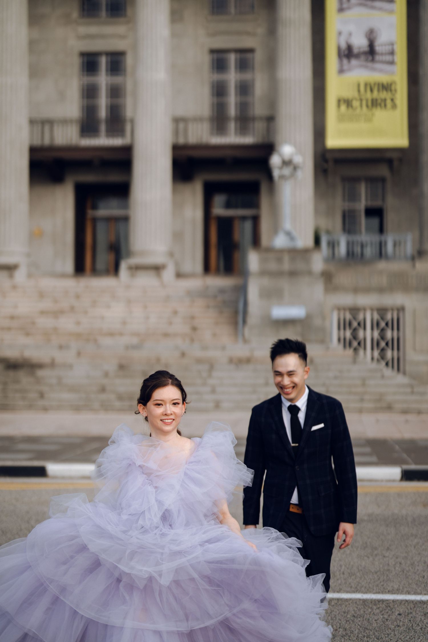 A couple runs playfully across stone steps, with the bride's lavender tulle gown flowing behind them.