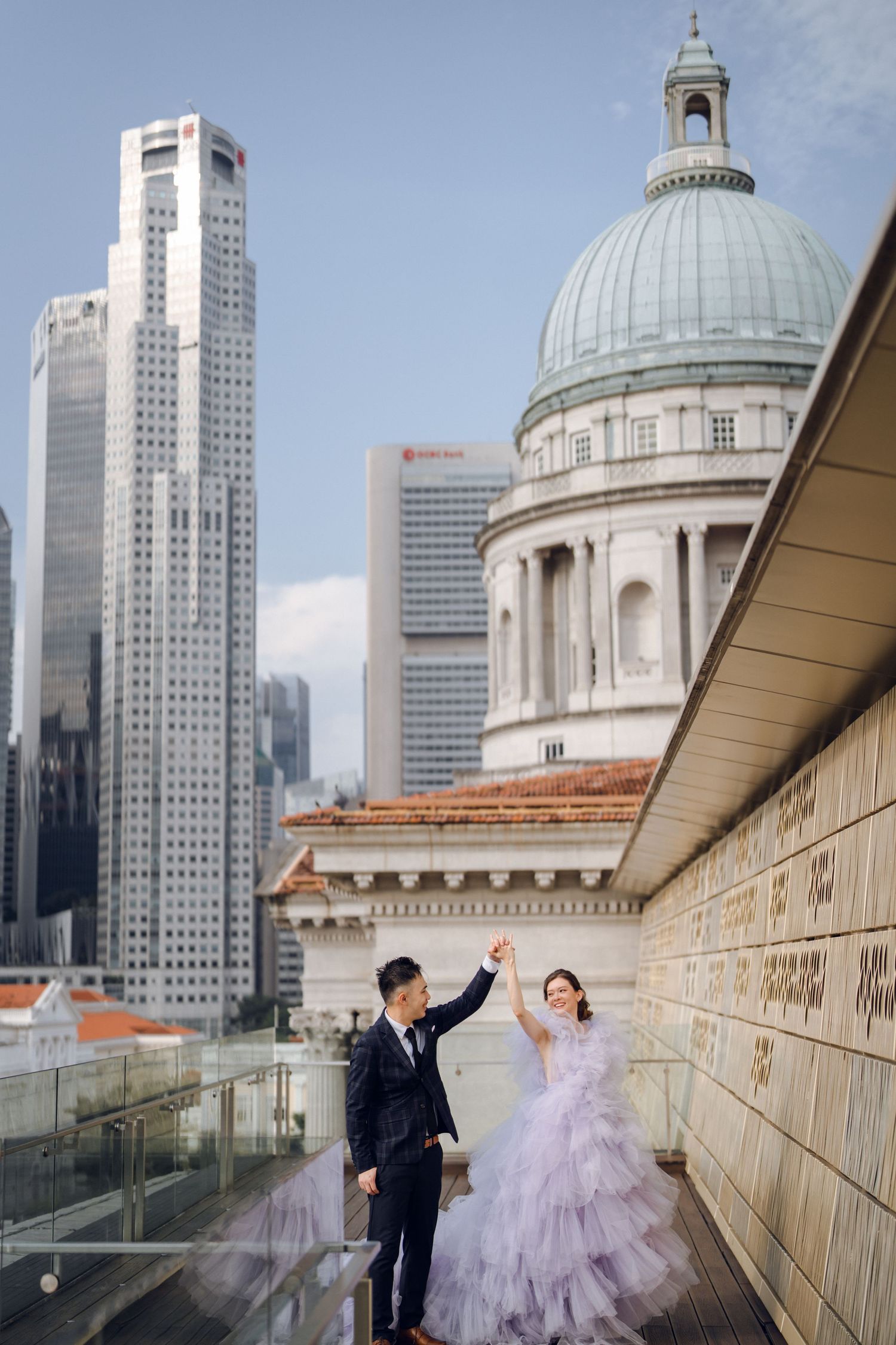 A romantic moment captured on an outdoor walkway with urban architecture and a domed building backdrop.