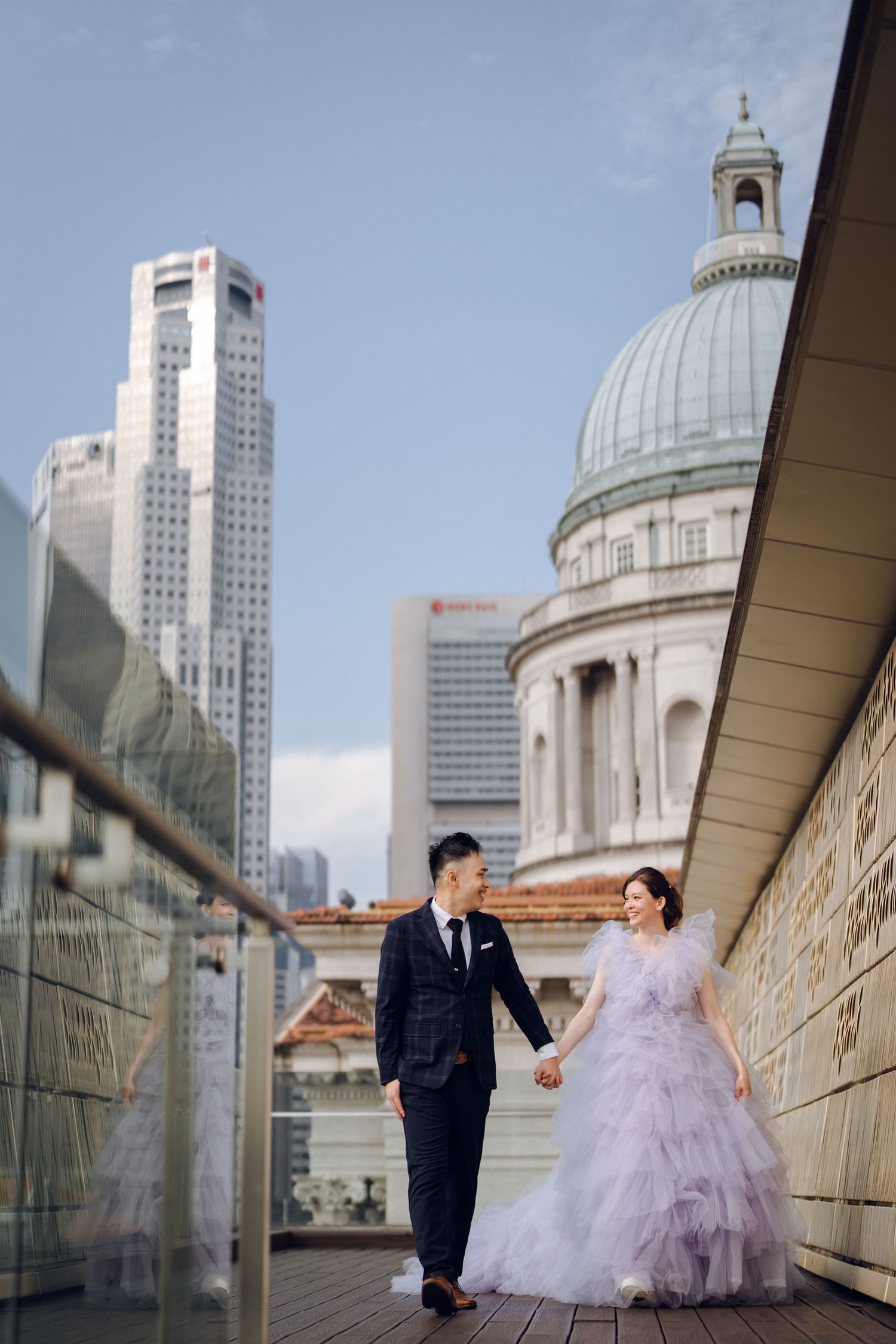 A couple poses on a walkway with city skyscrapers and a domed building in the background.
