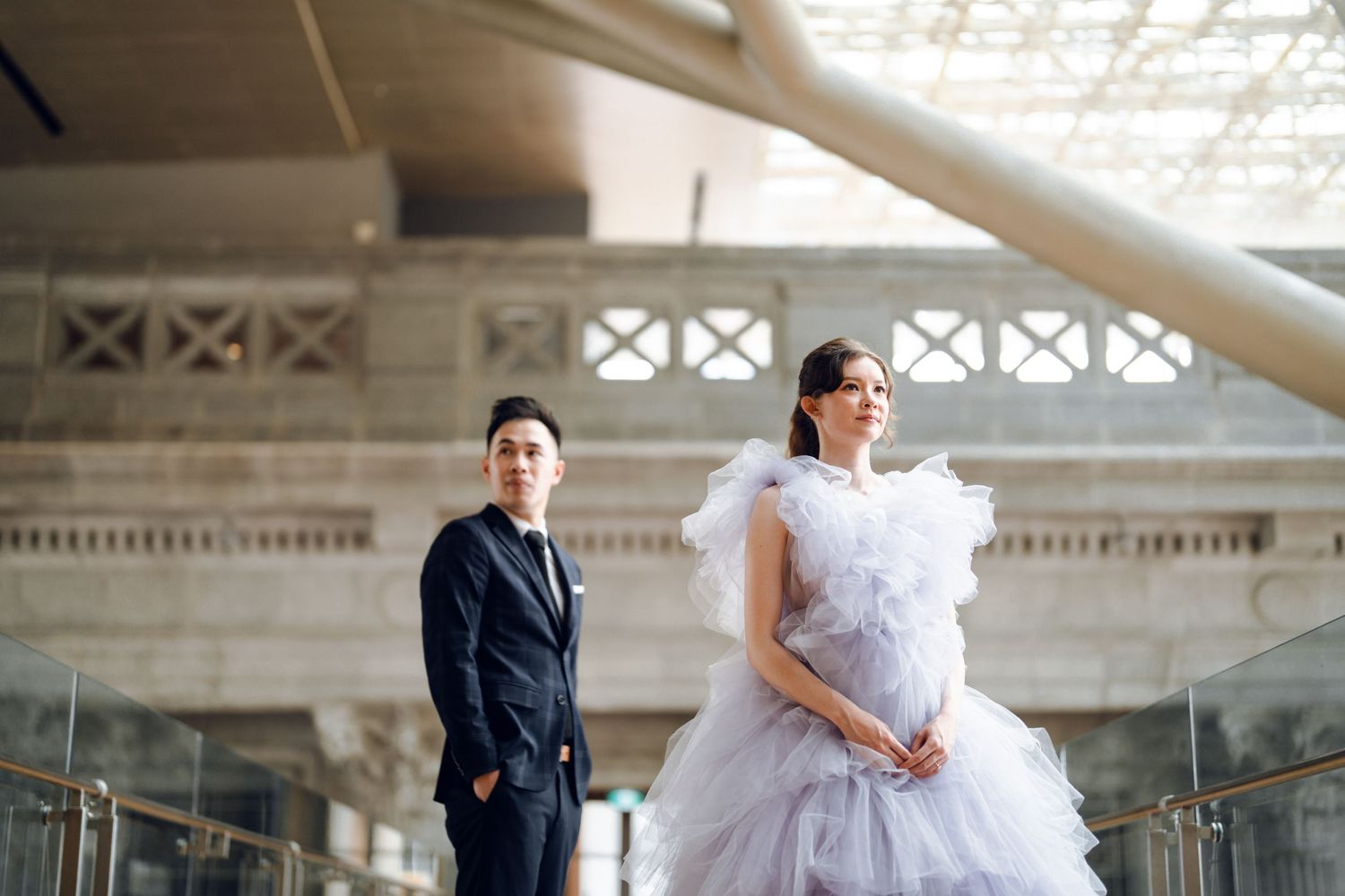 A couple shares a moment in an elegant indoor space with glass railings and classical columns.