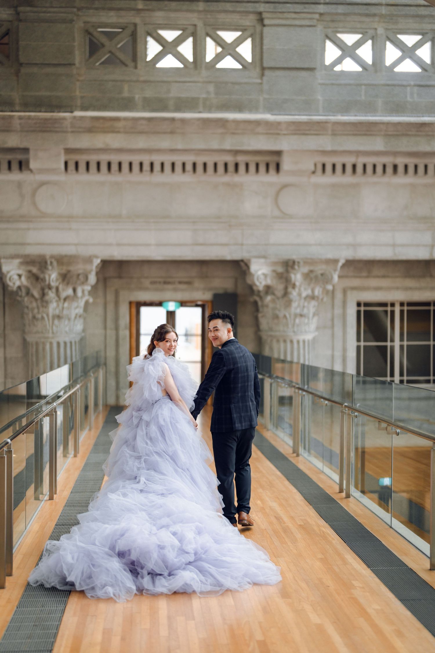 A couple poses in a grand indoor corridor with wooden floors and classical architectural details.