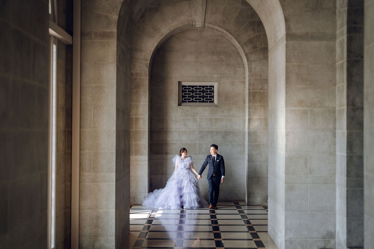 Romantic wedding photo in a stone hallway with natural light streaming through arches.