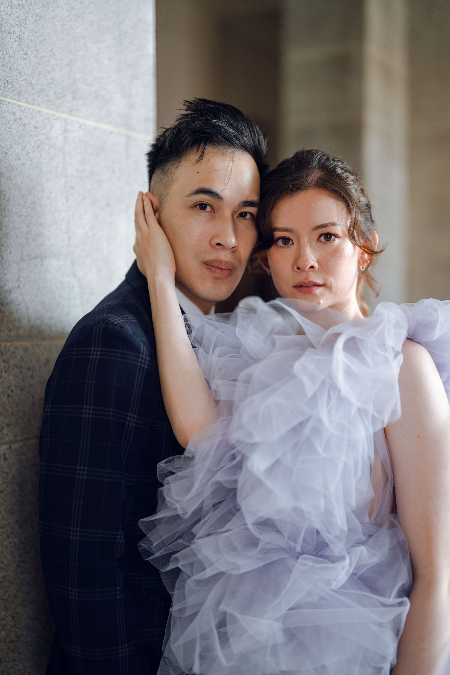 Intimate portrait of a couple in formal attire against a stone wall background.